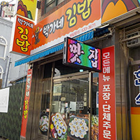 주황색 바탕에 박가네 김밥 이라고 적힌 간판 아래 입구인 유리문에 김밥 사진이 붙어있는 가게 외관의 모습