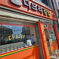 주황색 간판에 '다드리김밥'이라는 간판이 붙어있고 아래 가게 외부 유리에는 '한줄의 행복 다드리'라는 글이 부착되어있는 모습