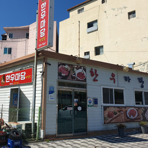 갈색 지붕에 하얀 멱으로 이루어진 가게의 간판에는 '한우마당'이라고 적혀있고 들어가는 문 상단과 오른쪽 벽면에 고기 사진이 붙어있다