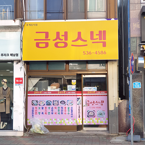 '금성스넥'이라고 적힌 노란 간판 아래 유리에 분홍색 바탕의 메뉴판이 붙어있는 가게 외관의 모습